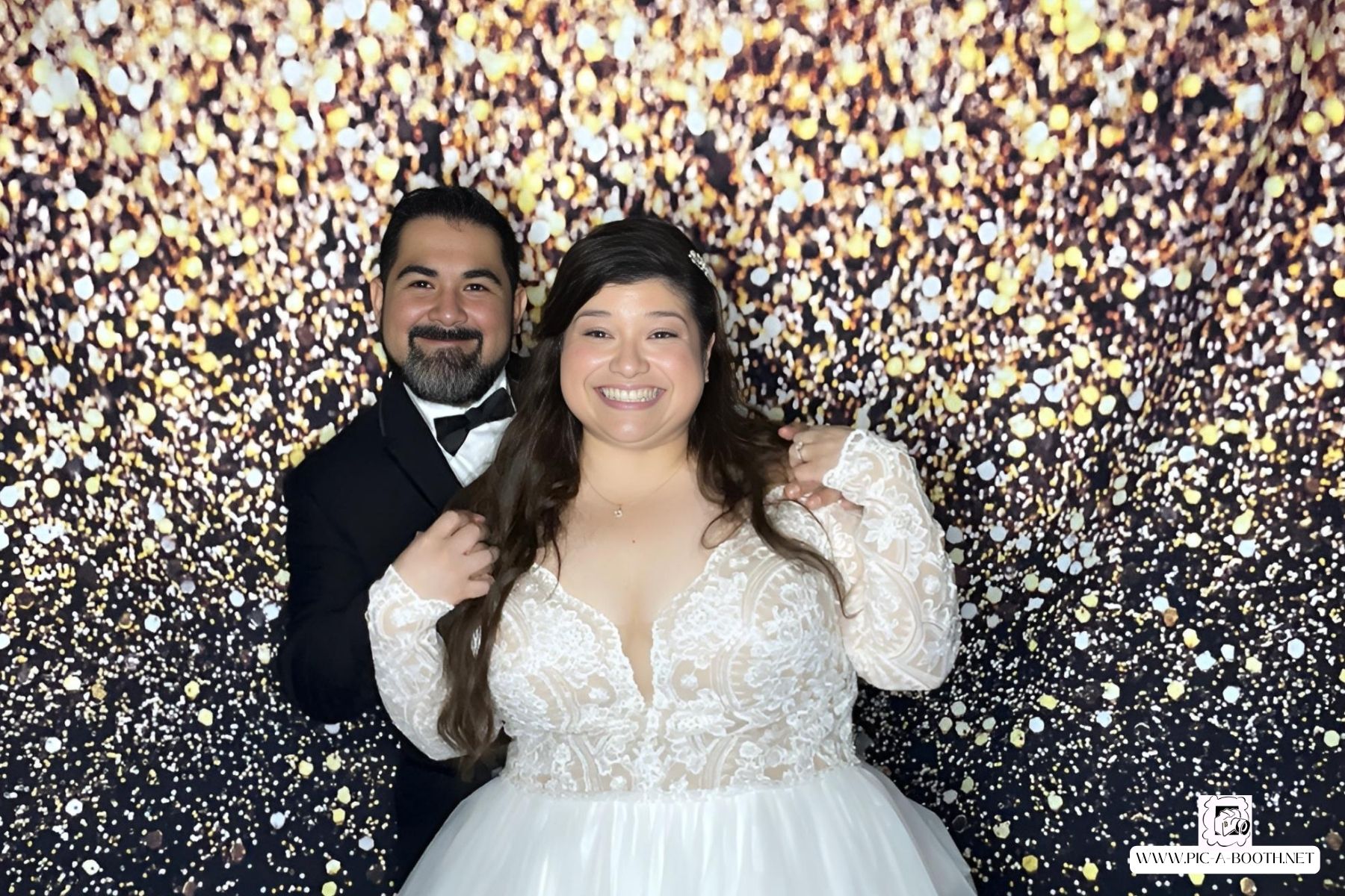Bride and groom smiling in front of gold sparkle photobooth backdrop